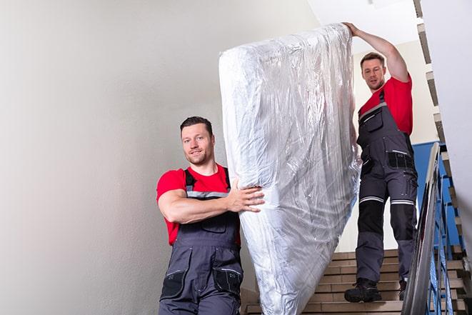 heavy lifting workers transporting a box spring out of a building in Concord